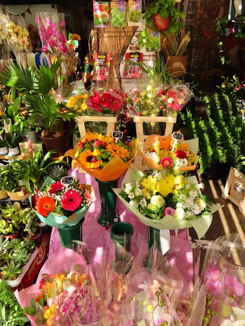 A display of fresh flower bouquets arranged in various vases and wrapping papers, featuring vibrant colors such as reds, yellows, pinks, and whites. The bouquets include a mix of roses, gerbera daisie