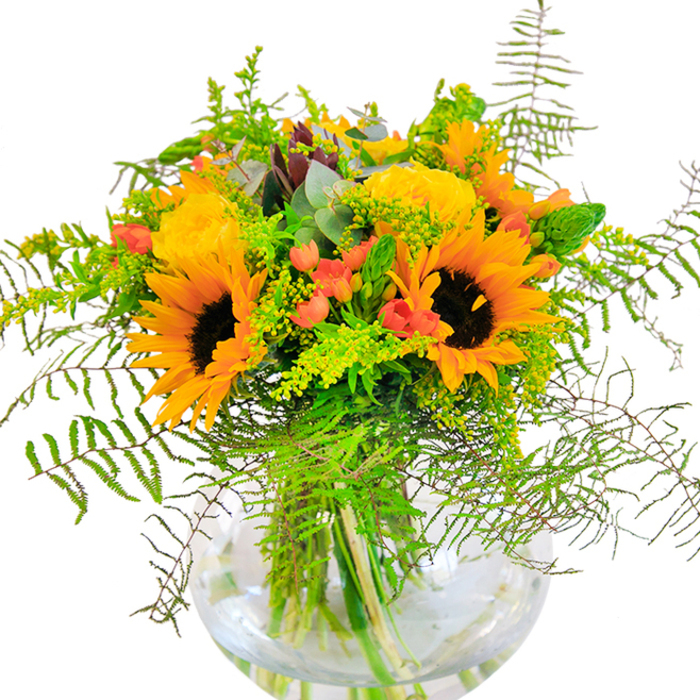 From the moment you glimpse this Byfleet-inspired bouquet, you're enveloped in the brilliance of its golden hues and intricate detail. Majestic sunflowers with bold, dark centers stretch outward in a display of optimism, their lush yellow petals a reminder of the blooming meadows and friendly faces you'll find near Byfleet's village hub. Interlaced among them, radiant yellow garden roses swirl open in elegant spirals, contributing a soft yet regal texture. Glossy, cherry-red hypericum berries are scattered throughout the design, their shine contrasting with the natural matte finish of the rose and sunflower petals. Long, feathery fern fronds and playful stems of light green filler weave throughout, echoing the lively greenery along the banks of the River Wey. Bluish eucalyptus and slender green spikes lend an airy, modern twist, enhancing the bouquet's layered effect. The bouquet is housed in a spherical glass vase, its transparency allowing viewers to admire the tangle of sturdy stems beneath-an emblem of fresh, local craftsmanship. Bathed in soft daylight, the overall composition glows with warmth, offering a sense of joy and peace that is perfect for birthdays, milestones, or a thoughtful delivery to any Byfleet neighbour seeking to uplift their day.