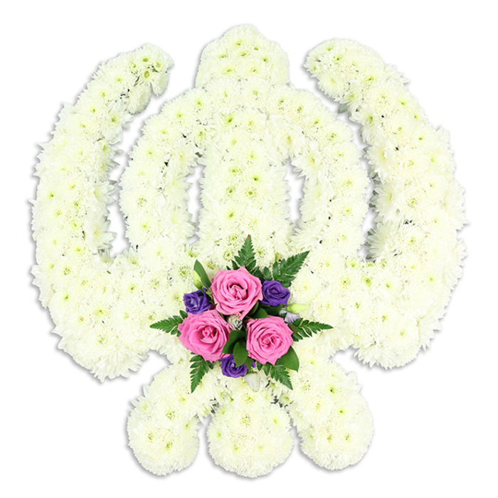 The photograph shows a striking Sikh Khanda floral tribute, carefully composed so that the entire emblem is visible against a crisp, white background, free from any distraction. The Khanda's distinctive elements are all present: an upright double-edged sword through the centre, a perfectly proportioned circular Chakra around it, and two gently arcing kirpans leaning outwards at the base. Rather than metal, these shapes are rendered in a dense covering of white chrysanthemum florets, each flower head small yet remarkably full. The petals overlap and layer to form a soft, plush texture that runs unbroken across the entire symbol, giving the arrangement a sense of purity, unity, and calm. The overall colour is a soothing white with a creamy undertone, which feels warm and respectful, very much in tune with the reflective mood of a funeral or memorial. Cradled at the very bottom centre, in the space formed by the crossing kirpans, sits a compact and vivid cluster of accent flowers. Three pink roses, fresh and open, tilt at slightly different angles so you can appreciate their spiralling hearts and rounded outer petals. They are framed by smaller, intense purple blooms-perhaps lisianthus or freesias-and a mix of lush green foliage, including fine fern fronds that add texture and movement. This small bouquet appears to glow against the white surround, symbolising personal love and remembrance dwelling within the strength of Sikh faith. A gentle shadow on the surface below adds depth and suggests a discreet stand. Created by expert florists serving Byfleet, accustomed to preparing meaningful tributes for local families from High Road to the quieter lanes near the River Wey, this floral Khanda would stand with quiet grace beside a casket or at a Gurdwara service, honouring a life with both cultural devotion and heartfelt tenderness.