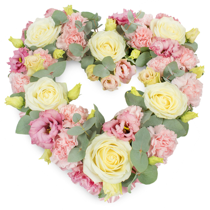 A soft, romantic heart-shaped floral tribute dominates this image, set cleanly against a white background so that every colour and petal detail is easy to imagine. The wreath is rich and full, its heart outline created entirely from layers of carefully chosen blooms. Creamy yellow and ivory roses appear throughout, their rounded shapes and tightly layered petals suggesting enduring love and devotion. Around them, pastel pink carnations create a gentle halo of ruffled texture, the many tiny folds of each petal adding movement and lightness to the design. Here and there, slightly deeper magenta and mauve lisianthus flowers emerge, more open and relaxed in their shape, adding both depth of colour and a soft, romantic feel, similar to the dusk glow along the River Wey not far from Byfleet. Threaded between the flowers are stems of silvery-green eucalyptus, their rounded leaves overlapping like small coins of muted colour, giving structure and calm to the heart's curves. Small yellow-green buds punctuate the pastel tones, providing a sense of freshness and life that gently tempers the sorrow associated with funeral flowers. The composition is dense yet balanced, each flower placed with intention, suggesting the work of a florist used to creating meaningful tributes for local families from Byfleet to neighbouring Surrey villages. The heart shape, with its gentle pastels and soothing greens, evokes sympathy, remembrance, and gratitude for a life well lived, making it a fitting choice for farewells, memorial services, or quiet anniversaries of loss, when a message of love and peace is needed most.