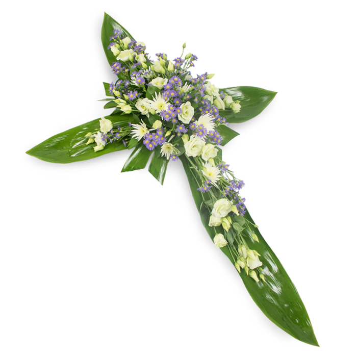 In this reverent cross arrangement the florist's hand is evident in every measured choice: broad, glossy tropical leaves form a verdant scaffold, their deep green and visible veins supplying strength and a satin sheen under gentle, diffused light. Resting atop that green canvas, clusters of soft white and creamy ivory lisianthus bloom with layered, petal-rich heads, while small, round white chrysanthemums or similar sprays provide texture and quiet luminosity where the arms meet the central intersection. Interspersed throughout are delicate sprays of pale lavender aster or limonium, tiny star-like blossoms that lend a whispered contrast and draw the eye gently outward from the centre. Fine, feathery foliage in a subtler green is threaded through the composition, easing transitions between leaf and bloom and enhancing the arrangement's living quality. The photo's slightly overhead angle reveals the cross's symmetry and the way the floral mass concentrates at the crossing, suggesting both the sheltering nature of the leaves and the tender fragility of the flowers. Lighting is soft and neutral, revealing the tactile differences - the leaves' smooth, almost waxy surface against the petals' soft, powdery matte - and evoking a faint, cool scent of green stems and faint floral sweetness. This piece is created for moments of remembrance: a dignified, peaceful tribute for funerals, memorial services, or church ceremonies in and around Byfleet and nearby Weybridge, conveying solace, faith and the quiet hope of comfort.