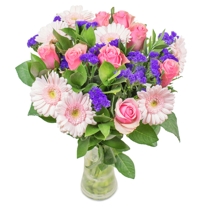 A lavish bouquet, elegantly displayed in a clear glass vase and set against a crisp white background, captures the spirit of Byfleet with its luminous palette. At its core, approximately seven to nine classic pink roses, many just beginning to unfurl, reveal graceful spiral formations in a range of gentle blush tones. These are complemented by a scattering of five to seven pale pink gerbera daisies, their round, textured faces and near-white centres softly reflecting Byfleet's tranquil charm. Sprigs of lively deep purple filler flowers-likely statice-punctuate the arrangement, adding drama and depth as they weave around the blushing blooms. Deep green foliage wraps the composition, recalling the lush greenery of Byfleet's river walks and parks. Every stem stands clearly in the fresh water of the glass vase, showcasing the arrangement's freshness and skilled placement. Ideal for gifting on occasions from birthdays to Mother's Day, or as a refined touch for an office by Brooklands or a cottage near Petersham Lock, this bouquet channels joy, celebration, and the everyday affection the Byfleet community is known for-a floral testament to beauty and local expertise.